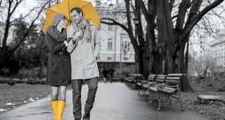 Paar mit gelbem Regenschirm geht im Regen spazieren