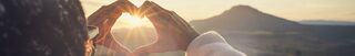 Eine Person formt ihre Hände zu einem Herzen vor dem Sonnenuntergang