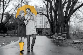 Paar mit gelbem Regenschirm geht im Regen spazieren